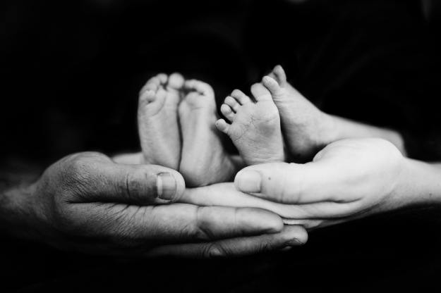 Black and white image shows adult hands cradling the feet of a newborn.